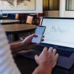 Stock Trading - person using smartphone and MacBook Pro