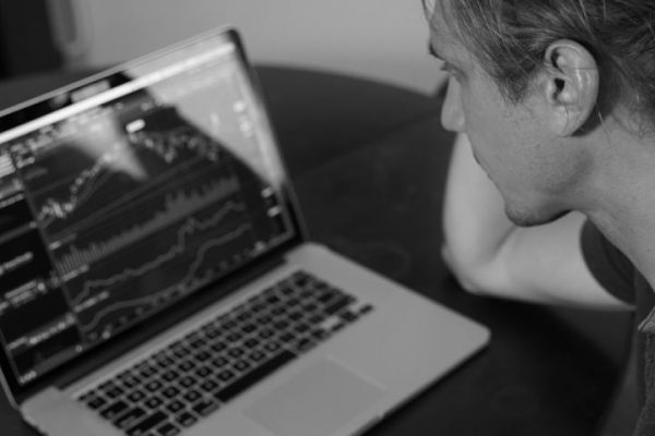 Stock Trading - grayscale photo of man looking at macbook pro