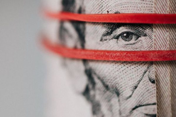 Economies - Closeup of rolled United States five dollar bills tightened with red rubber band