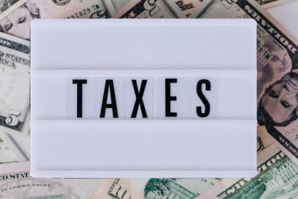 Tax - Top view of white vintage light box with TAXES inscription placed on stack of USA dollar bills on white surface