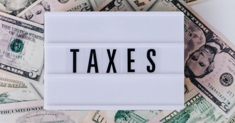 Tax - Top view of white vintage light box with TAXES inscription placed on stack of USA dollar bills on white surface