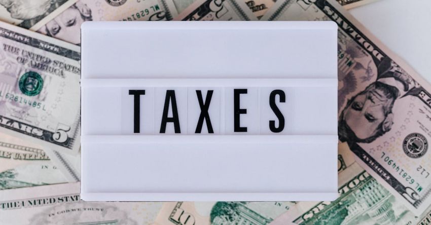 Tax - Top view of white vintage light box with TAXES inscription placed on stack of USA dollar bills on white surface