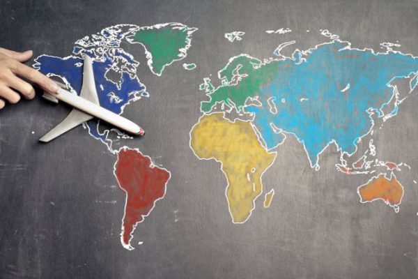 Globalization - Top view of crop anonymous person holding toy airplane on colorful world map drawn on chalkboard